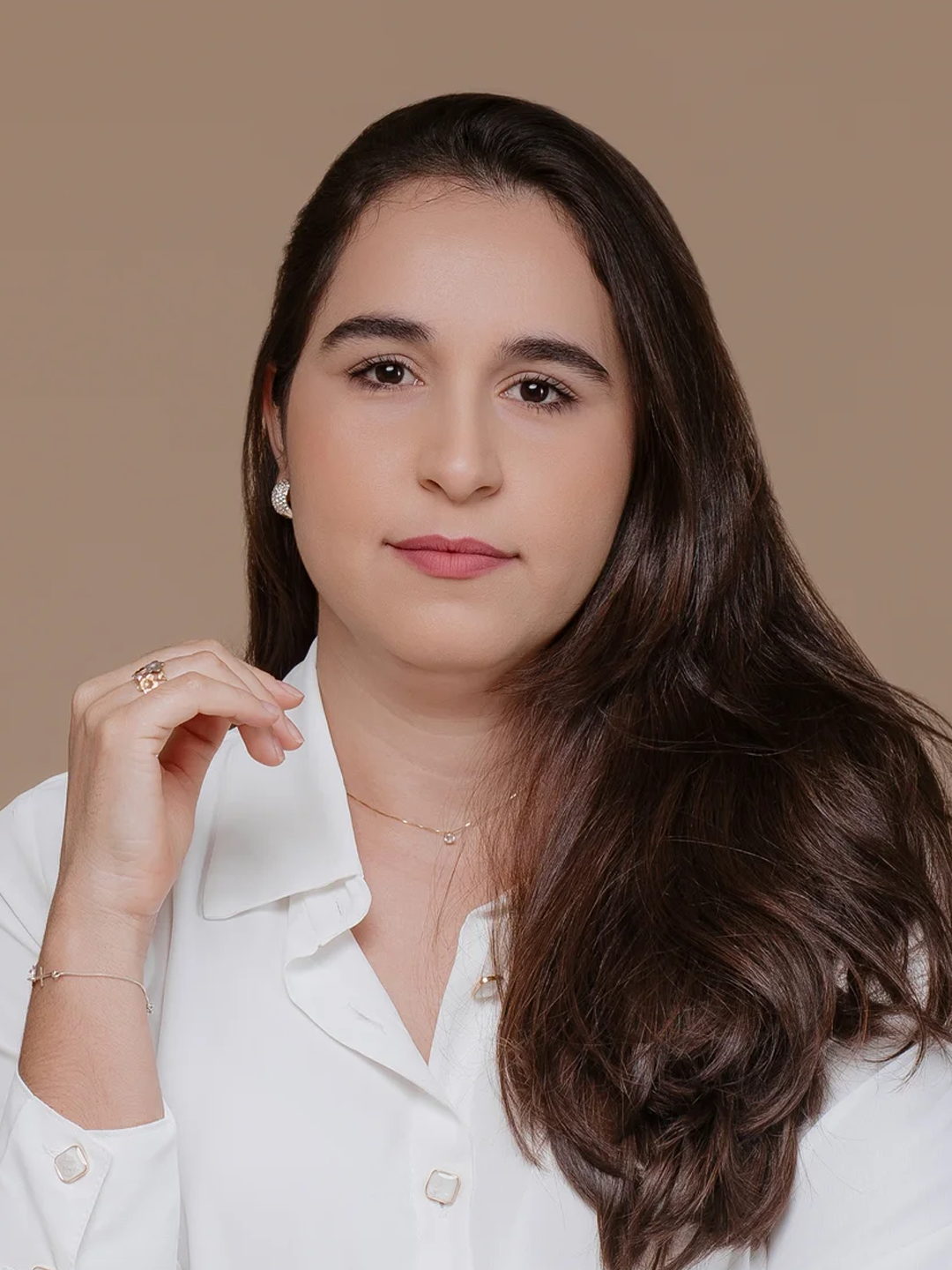 Foto de mulher sorrindo, usando óculos, fundo claro, cabelo castanho e ondulado